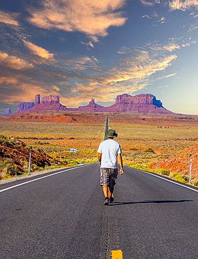 A young man in a white shirt walking on the road to Monument Valley in sunset. Utah