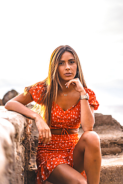 A young brunette Caucasian woman in a red dress on the beach of Itzurrun in the town of Zumaia, Gipuzkoa. Basque Country. Lifestyle session, enjoying the sea by stairs