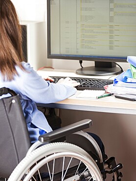 Invalid or disabled young business woman person sitting wheelchair working office desk computer