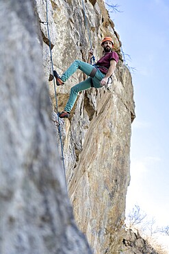 A young man climbs a challenging cliff route, secured by a rope, showcasing strength and determination against the rugged rock face under a clear sky, capturing the thrill and intensity of the ascent