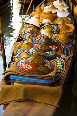 Many colorful wicker hats in a traditional conical asian style are stored in a boat at the famous tourist destination of Damoen Saduak floating market in Thailand