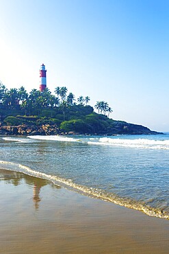 Lighthouse standing above the rocky outcrop above the ocean waves at Kovalam Beach in Kerala, India. Vertical