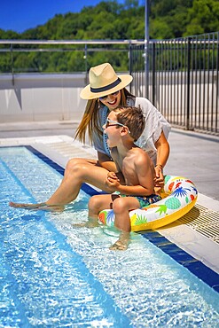 Vertical photo full length of a caucasian mother and kid playing sitting on a swimming pool