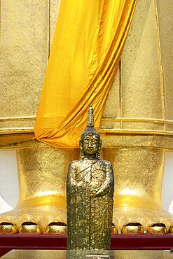 Buddha figure decorated with gold leaf in front of a 32 metre high standing Buddha statue, Wat Intharawihan, Bangkok, Thailand, Asia