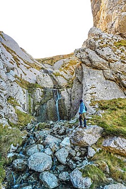 Hiker in blue jacket navigating rocky landscape near a small waterfall on mount txindoki, showcasing the rugged beauty of gipuzkoa, basque country