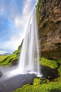 Sunny day in Iceland. Seljalandsfoss waterfall in July. Passage under the waterfall
