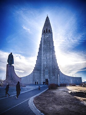 Tourists walking on pavement near magnificent Lutheran church building on beautiful day in Reykjavik, Iceland