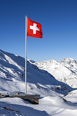 Swiss flag in front of mountain landscape in winter, mountain panorama with the peaks of the Bergüner Stöcke Tinzenhorn and Piz Ela, view at the Keschhütte in winter, Bündner Haute Route, Albula Alps, Rhaetian Alps, Grisons, Eastern Switzerland, Switzerland