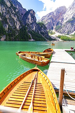 Several wooden boats are moored to a jetty on a calm, emerald-green mountain lake, Lake Braies, South Tyrol, Dolomites, Italy