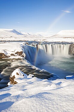 Rainbow at the waterfall Góðafoss, Godafoss in winter with snow and ice, water of the Skjálfandafljót river, Norðurland vestra, Northern Iceland, Iceland