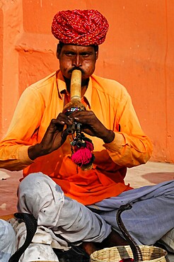 Jaipur, Rajasthan, India, Asia, A snake charmer plays a traditional wind instrument in front of a basket in bright orange-coloured clothing, North India