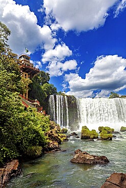 Impressive waterfall with neighbouring building and flag, blue sky and lush greenery, The Iguazu Falls between Argentina and Brazil