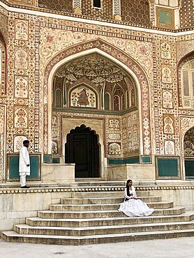 Decorated palace entrance with stairs and two people in traditional dress in a historic building, Amber Fort, Jaipur, Rajasthan, India