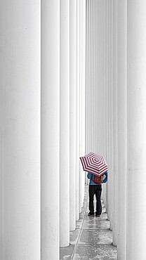 Person with a striped umbrella in a corridor of white columns, Philharmonie Luxembourg, Concert Hall, Grand Duchy of Luxembourg