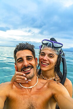 Happy couple taking a selfie while snorkeling in tropical turquoise water, enjoying their vacation in a beautiful seascape
