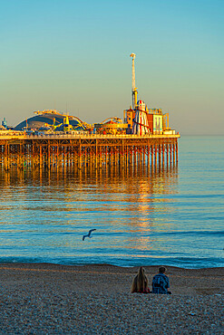 View of couple on beach and Brighton Palace Pier at sunset, Brighton, East Sussex, England, United Kingdom, Europe