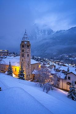 View of Church of Saint Pantalon and the snow covered town centre and mountainous background in winter, Courmayeur, Aosta Valley, Italy, Europe