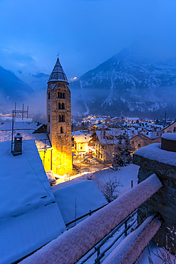 View of Church of Saint Pantalon and the snow covered town centre and mountainous background in winter at dusk, Courmayeur, Aosta Valley, Italy, Europe