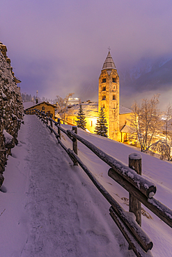 View of Church of Saint Pantalon and the snow covered town centre and mountainous background in winter at dusk, Courmayeur, Aosta Valley, Italy, Europe