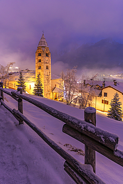 View of Church of Saint Pantalon and the snow covered town centre and mountainous background in winter at dusk, Courmayeur, Aosta Valley, Italy, Europe