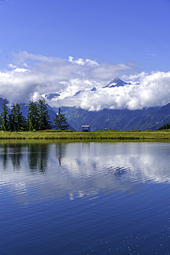 View of reflection of mountains and clouds in Plettsaukopf Reservoir on a sunny day, Bruckberg, Salzburg, Austria, Europe