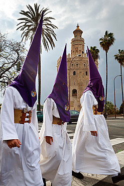 Penitents during Semana Santa (Holy Week) beneath Torre del Oro, Seville, Andalucia, Spain, Europe