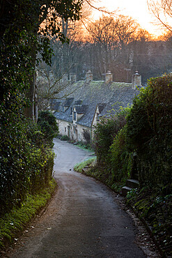 View down lane to Arlington Row Cotswold stone cottages at dawn, Bibury, Cotswolds, Gloucestershire, England, United Kingdom