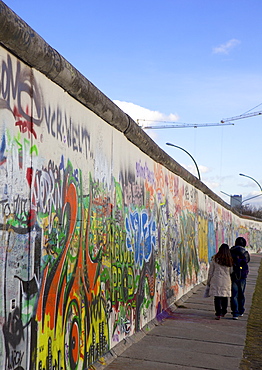 Couple walking along the East Side Gallery Berlin Wall mural, Berlin, Germany, Europe 