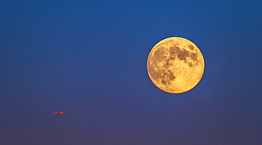 Plane flying across clear sky with full moon