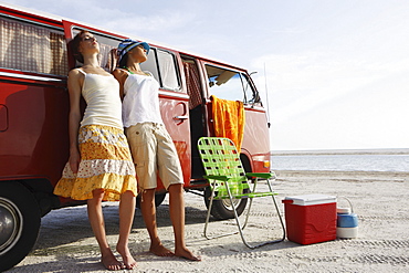 Young women leaning against van on beach