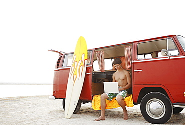 Young surfer using laptop in van on beach