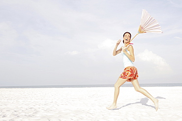 Girl running on beach with umbrella