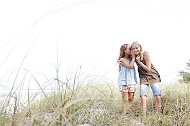 Girls telling secrets on grassy sand dune