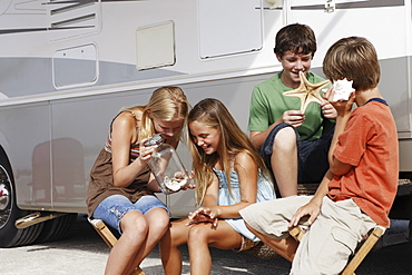 Children looking at seashell collection by motor home