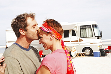 Couple kissing by motor home on beach