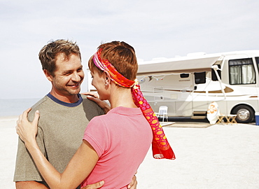 Couple hugging by motor home on beach