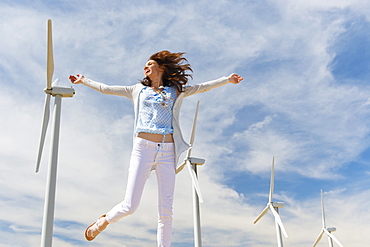 Woman jumping in front of wind turbines