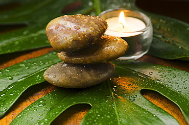 Spa stones and candle on tropical leaf, studio shot