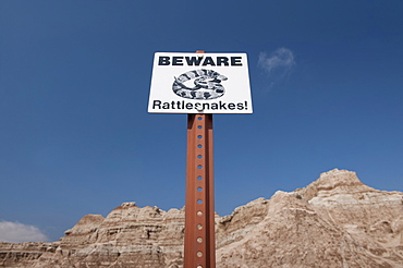 USA, South Dakota, Badlands National Park, Rattlesnake warning sign against sky, mountain in background