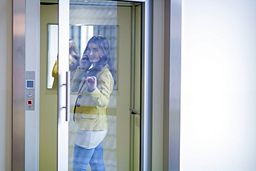 Woman opening glass door and talking on cell phone