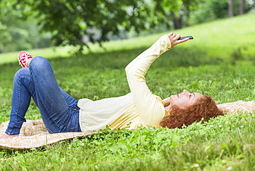 Woman lying on grass in park and using mobile phone