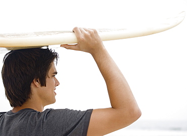 Man carrying surfboard on head 