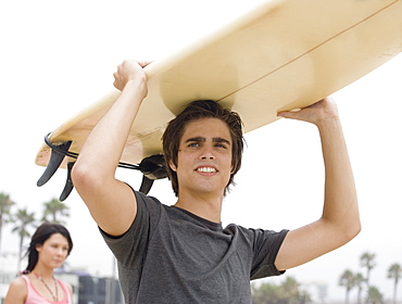 Man carrying surfboard on head 