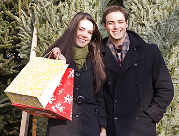 Couple with shopping bags in front of Christmas trees