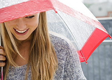 Smiling young woman with umbrella in rain