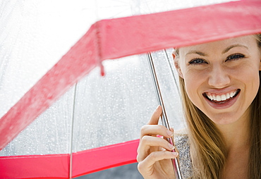 Portrait of smiling young woman with umbrella in rain