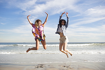 Two young women jumping on beach, Rockaway Beach, New York