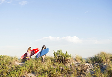 Two female surfers walking on beach, Rockaway Beach, New York