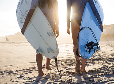 Two female surfers walking on beach, Rockaway Beach, New York