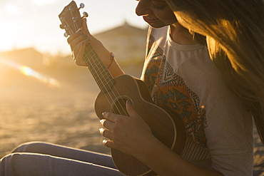 Woman playing ukulele at sunset, Rockaway Beach, New York